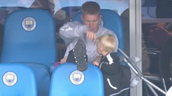 Kevin De Bruyne's cute son tries to climb over crocked Man City star's leg as he rests injured knee during Huddersfield clash